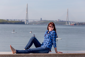 Portrait of nice young caucasian woman in casual dress on sea embankment. Famous Russky Bridge is on background. Russia, Vladivostok, Russky Island.