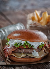 burger with bacon and cutlet with cheese, tomato, greens. served with fries and beer on a wooden table