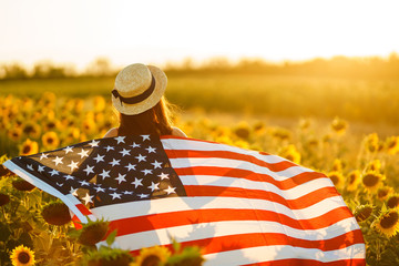 Beautiful girl in hat with the American flag in a sunflower field. 4th of July. Fourth of July....