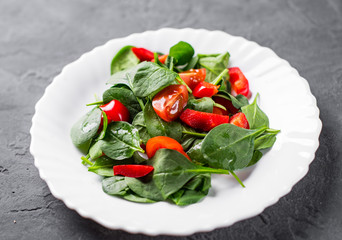 spinach salad with pepper and tomatoes in white plate on Dark grey black slate background