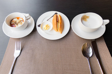 Breakfast meal on the table; soft-boiled egg, vietnamese baguette and coffee on table setting with table mat copy space. 