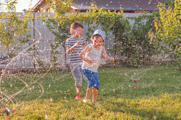 Siblings having fun outdoor in the summer. School holidays concept. Summer holidays background. Interesting games for children outdoor. Happy boy plays with water drops on sunny summer day