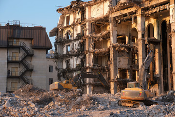 Building demolition with hydraulic excavator. Dismantle of destructed house ruins at bright sunsest