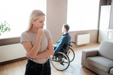 Young man sit with special needs sit on wheelchair and look on window. Woman stand in front and...
