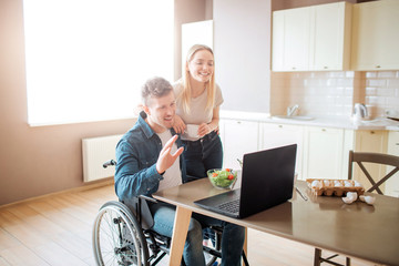 Happy cheerful young man sit at table and look on laptop. Guy with disability and inclusiveness....