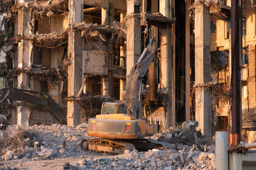 Fototapeta premium Building demolition with hydraulic excavator. Dismantle of destructed house ruins at bright sunsest