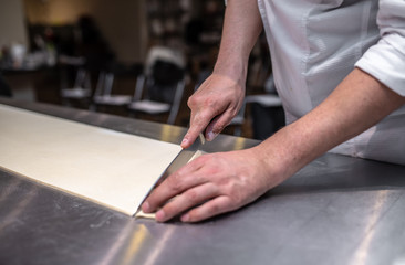 Producing classic french croissants at the bakery shop. Chef is cutting dough by knife.