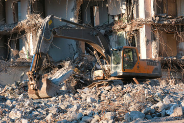 Building demolition with hydraulic excavator. Dismantle of destructed house ruins at bright sunsest