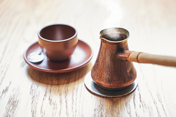 Hot coffee with steam in oriental Turkish style served in cezve, a small long-handled pot with a pouring lip and cup on a wooden table