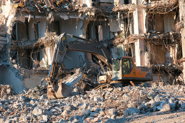 Building demolition with hydraulic excavator. Dismantle of destructed house ruins at bright sunsest