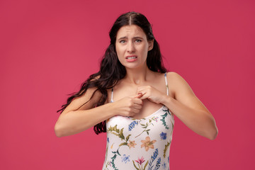 Portrait of a pretty young woman in a light dress standing on pink background in studio. People sincere emotions.