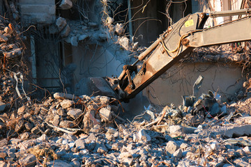 Building demolition with hydraulic excavator. Dismantle of destructed house ruins at bright sunsest