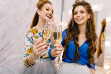 Two glasses of champagne holding by attractive happy young women having fun in hairdresser salon. Expressing true positive emotions, smiling, chilling, luxury lifestyle, fashionable models