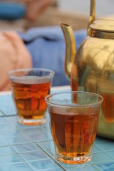 Oriental glass cup with tea on the background of a golden teapot on a ceramic table