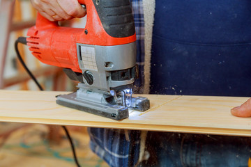 Man cutting a plank with a jigsaw machine sawing wood board