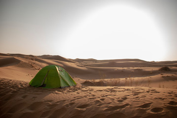 Fototapeta na wymiar A big sun shines in the sky on a green tent on desert