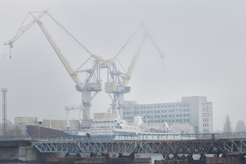 Fototapeta na wymiar Lifting cargo cranes and ship in sea port. Foggy industrial landscape.