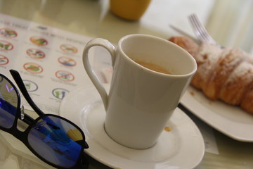 Breakfast composition in a cafe from a cup of coffee, a croissant on a plate and glasses