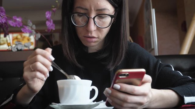 Young wonam use mobile phone while sitting in comfortable coffee shop during work break, charming happy female reading fashion news on cell telephone during breakfast in restaurant.