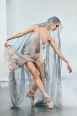 Beautiful dark-haired Arabian female dancer dancing in grey transparent costume with cape on head in white studio