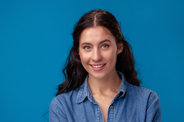 Close-up portrait of an attractive brunette girl with long curly hair posing on a blue background.