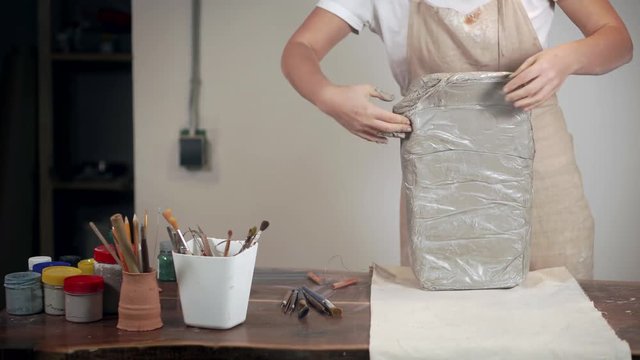 Woman is unpackaging clay for modeling in working studio,