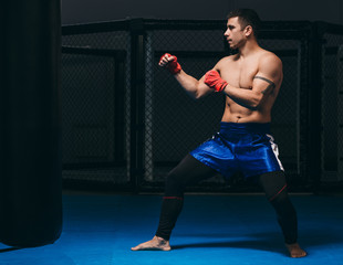 Martial arts of Muay Thai, Thai Boxing, Muay Thai. Barefoot Fighter training indoors dressed in blue boxer shorts and having his fists protected with red bandage.