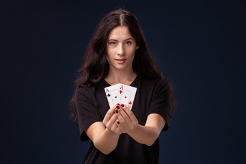 Curly hair brunette is posing with playing cards in her hands. Poker concept on a black background. Casino.