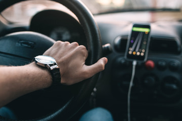 driver with a wristwatch rides through the city using a navigator on a smartphone on a sunny day.