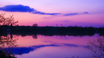 Nice symmetry of clouds reflected in the water of a lake. Very colorful sunrise in a beautiful landscape