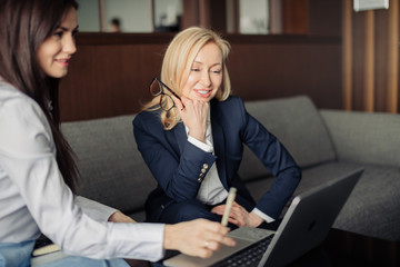 Two elegant classic business women, female partners in formal wear having conversation, planning project budget while sitting on couch in office