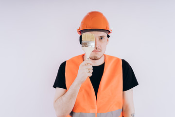 Fototapeta na wymiar Man in orange workwear with coloring brush Portrait of young male in protective uniform with paintbrush looking at camera and smiling on white background