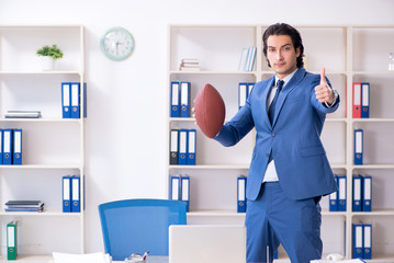 Young handsome businessman with rugby ball in the office