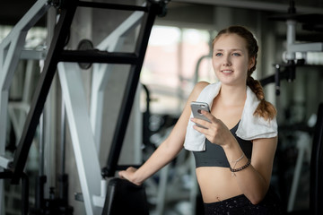 Fototapeta na wymiar Happy Young attractive women fitness using smartphone resting in gym during morning exercise. Relaxation after hard workout in gym. Healthy sports lifestyle, Fitness concept.