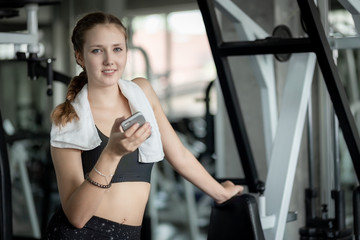 Fototapeta premium Happy Young attractive women fitness using smartphone resting in gym during morning exercise. Relaxation after hard workout in gym. Healthy sports lifestyle, Fitness concept.