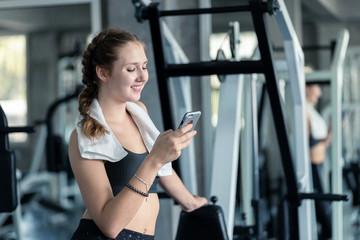 Fototapeta na wymiar Happy Young attractive women fitness using smartphone resting in gym during morning exercise. Relaxation after hard workout in gym. Healthy sports lifestyle, Fitness concept.