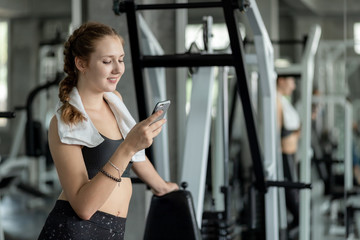 Plakat Happy Young attractive women fitness using smartphone resting in gym during morning exercise. Relaxation after hard workout in gym. Healthy sports lifestyle, Fitness concept.