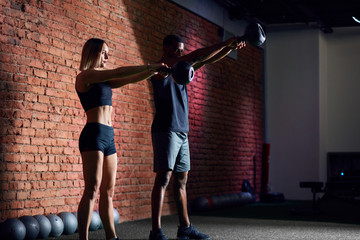 Young caucasian woman athlete working out with kettlebells with the help of personal trainer during body core cross fit workout