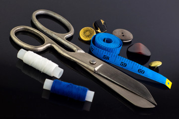 vintage big seamstress scissors, measuring blue tape and buttons on black background. short focus