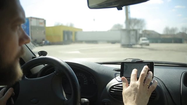 A man gets into the car and turns on the navigator on the smartphone
