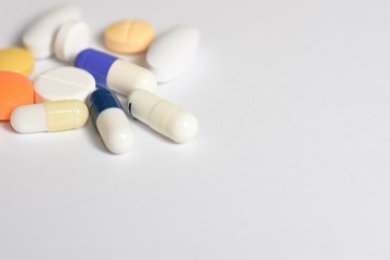 A close-up photo of various medical pills and capsules spilt on white background