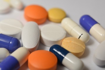A close-up photo of various medical pills and capsules spilt on white background