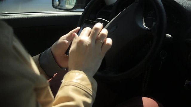 A man with a beard sits in a car and writes an SMS message on a smartphone
