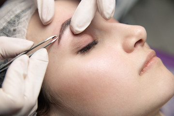 Process of making eyebrows by tweezers. Pretty woman with closed eyes on the procedure
