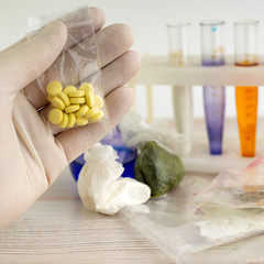 study of synthetic drugs: a scientist holds a sample of a new drug above the table with other samples, short focus