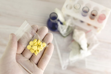invention of synthetic narcotic drugs: a person holds a sample of a new drug above the table with other samples, short focus