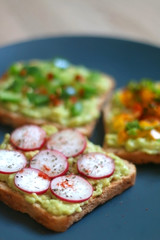 Three slices of toast with mashed avocado and various vegetable and herb toppings. Selective focus.