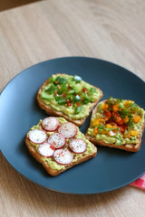 Three slices of toast with mashed avocado and various vegetable and herb toppings. Selective focus.