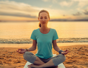 Fototapeta na wymiar Young woman meditating in pose of lotus on yoga mat on beach.