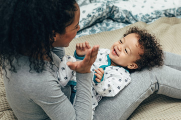 Happy child lying on mother hips. Mother playing with son.